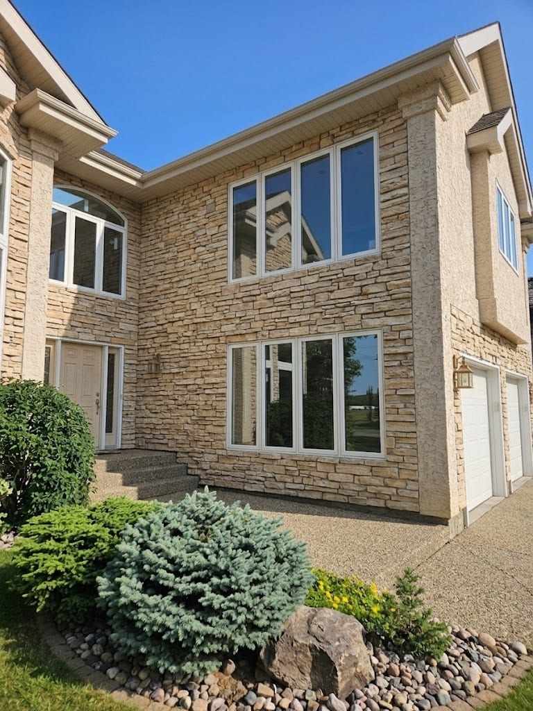 A two-storey house clad in stacked stone and stucco, with two groups of three tall white-framed casement windows one above the other, an arch-topped window over the entry to the left, and a white panelled front door.